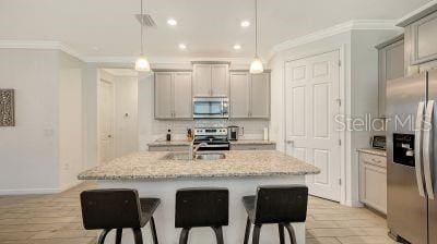 kitchen featuring hanging light fixtures, stainless steel appliances, a kitchen island with sink, and gray cabinetry