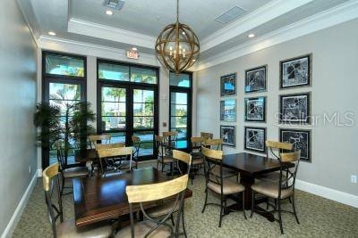 dining area featuring french doors, a raised ceiling, carpet floors, a chandelier, and ornamental molding