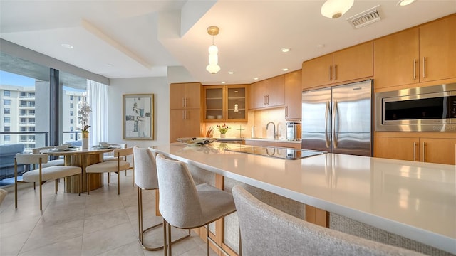 kitchen with a kitchen breakfast bar, expansive windows, sink, hanging light fixtures, and built in appliances