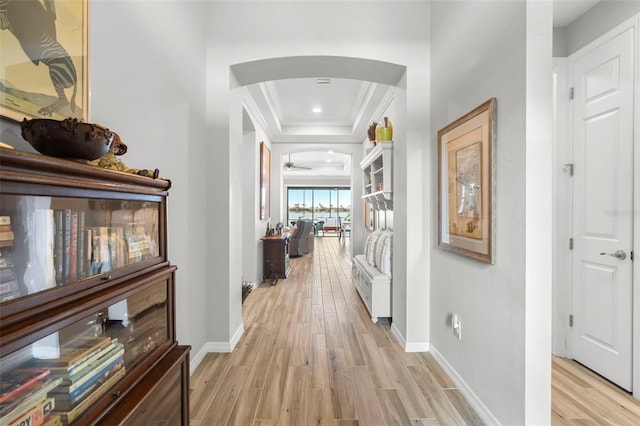 hallway with a tray ceiling, crown molding, and light wood-type flooring