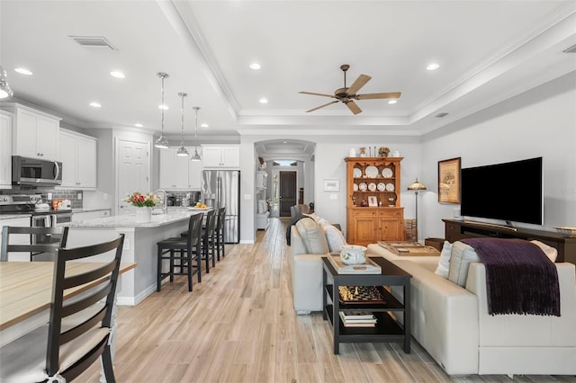 living room featuring ceiling fan, a raised ceiling, and ornamental molding