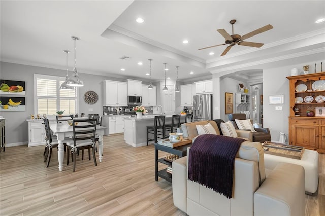 living room with a raised ceiling, ceiling fan, sink, and ornamental molding