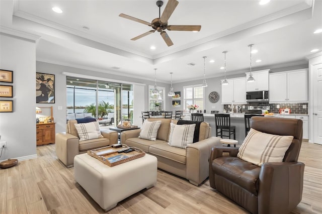 living room with a raised ceiling, ceiling fan, crown molding, and light hardwood / wood-style floors