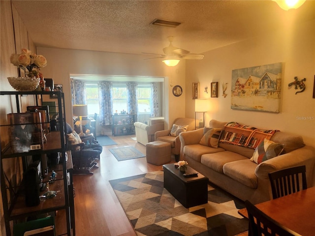 living room with ceiling fan, a textured ceiling, and hardwood / wood-style flooring