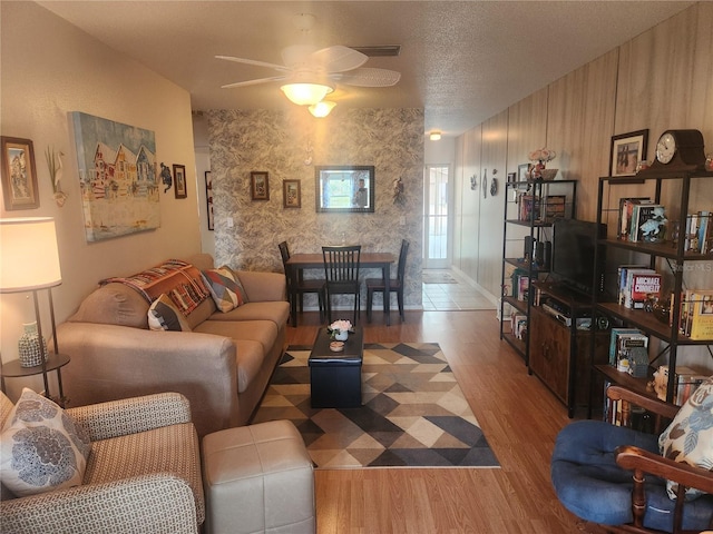 living room with ceiling fan, a textured ceiling, and light wood-type flooring