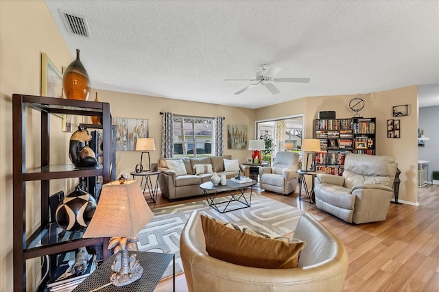 living room with a textured ceiling, light wood-type flooring, and ceiling fan