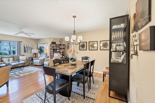 dining space featuring ceiling fan with notable chandelier, a textured ceiling, and light hardwood / wood-style floors