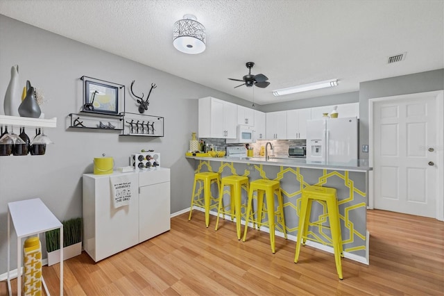 kitchen with white cabinets, a kitchen bar, white appliances, and kitchen peninsula