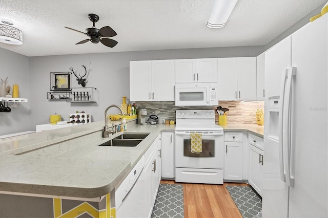 kitchen featuring sink, white appliances, white cabinetry, and kitchen peninsula