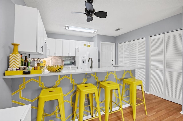 kitchen featuring white cabinets, a kitchen bar, light hardwood / wood-style floors, kitchen peninsula, and white refrigerator with ice dispenser