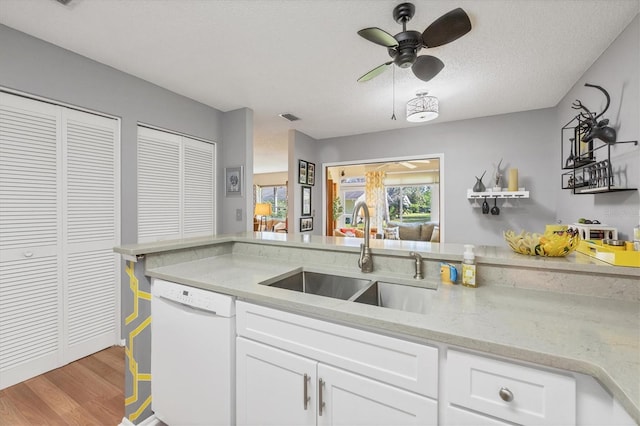 kitchen with a textured ceiling, light wood-type flooring, white cabinetry, white dishwasher, and sink