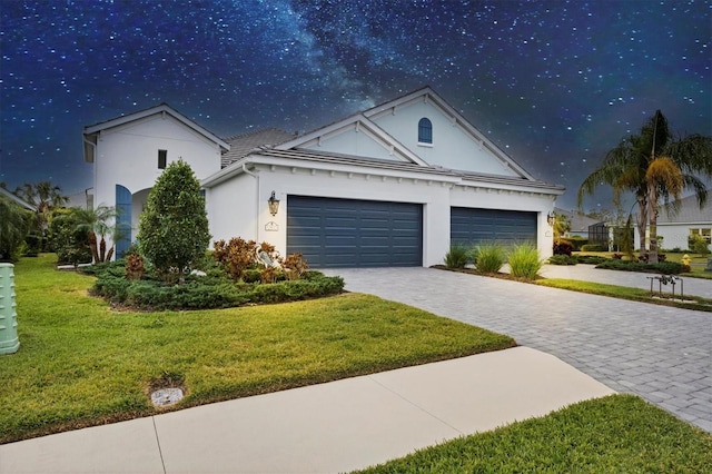 view of front of property featuring a garage, stucco siding, decorative driveway, and a front yard