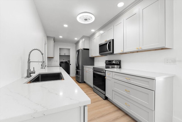 kitchen featuring white cabinetry, sink, light stone counters, appliances with stainless steel finishes, and light wood-type flooring