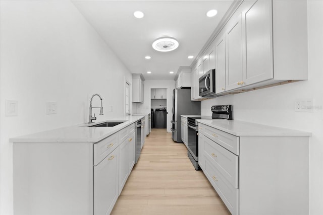 kitchen with white cabinetry, sink, light hardwood / wood-style floors, washer and clothes dryer, and appliances with stainless steel finishes