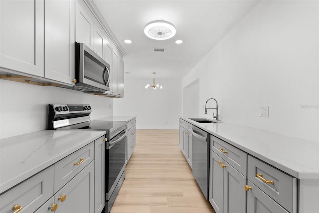 kitchen featuring light stone countertops, sink, hanging light fixtures, gray cabinets, and appliances with stainless steel finishes