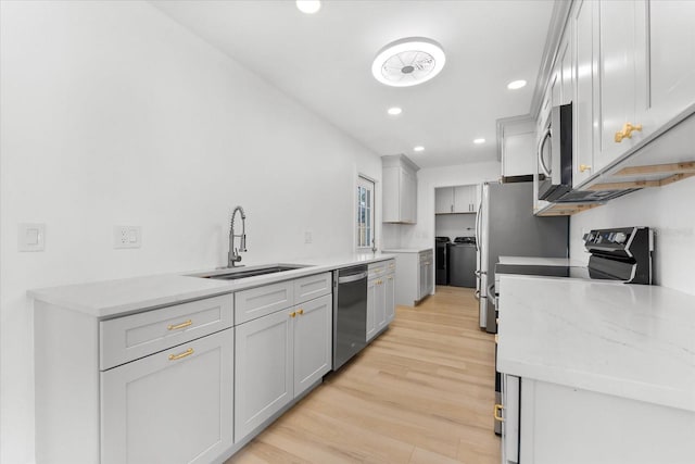 kitchen featuring light stone countertops, appliances with stainless steel finishes, light wood-type flooring, sink, and separate washer and dryer