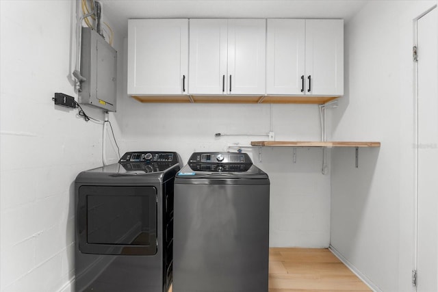 clothes washing area featuring washer and dryer, light hardwood / wood-style floors, cabinets, and electric panel