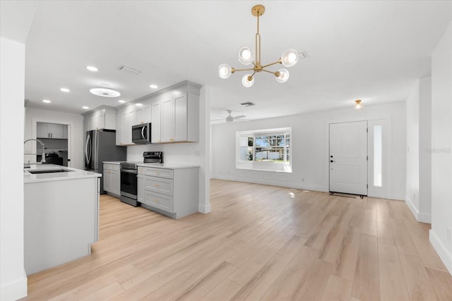 kitchen featuring sink, light wood-type flooring, ceiling fan with notable chandelier, and appliances with stainless steel finishes