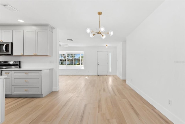 kitchen featuring pendant lighting, ceiling fan with notable chandelier, light hardwood / wood-style flooring, gray cabinets, and stainless steel appliances