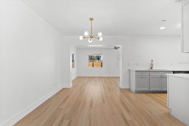 unfurnished dining area with sink, ceiling fan with notable chandelier, and light hardwood / wood-style flooring