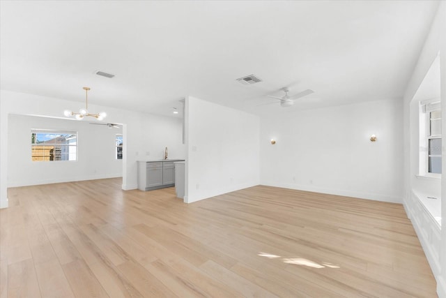 unfurnished living room with ceiling fan with notable chandelier, light hardwood / wood-style floors, and sink