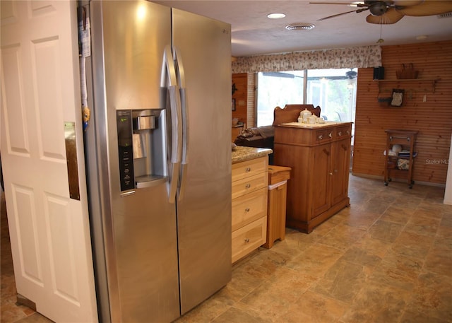 kitchen featuring stainless steel fridge, a kitchen island, ceiling fan, and wood walls