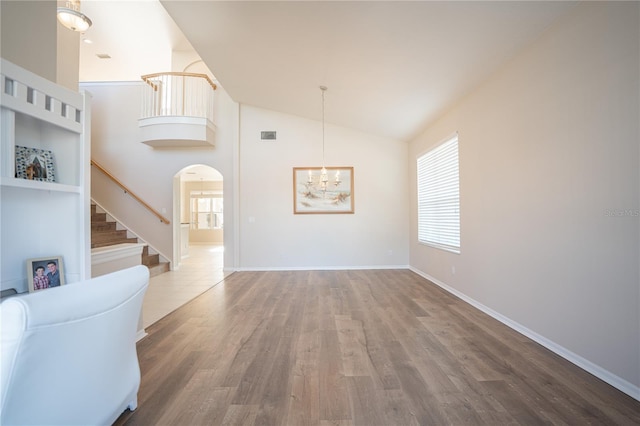 unfurnished living room featuring a notable chandelier, wood-type flooring, and lofted ceiling