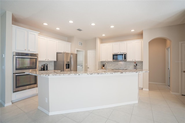 kitchen with tasteful backsplash, a kitchen island with sink, white cabinets, and appliances with stainless steel finishes