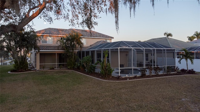 back house at dusk with a lanai and a lawn