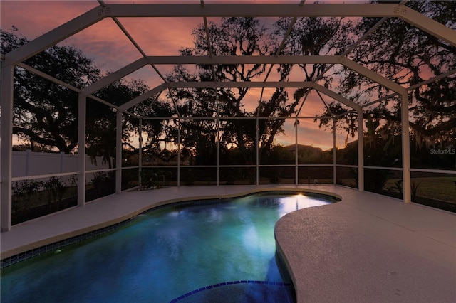 pool at dusk featuring glass enclosure and a patio area