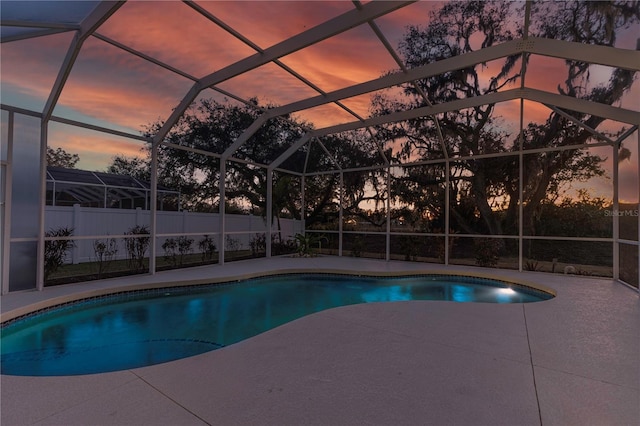 pool at dusk featuring glass enclosure and a patio