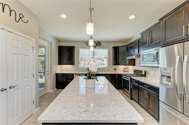 kitchen with pendant lighting, appliances with stainless steel finishes, a kitchen island, plenty of natural light, and light stone counters