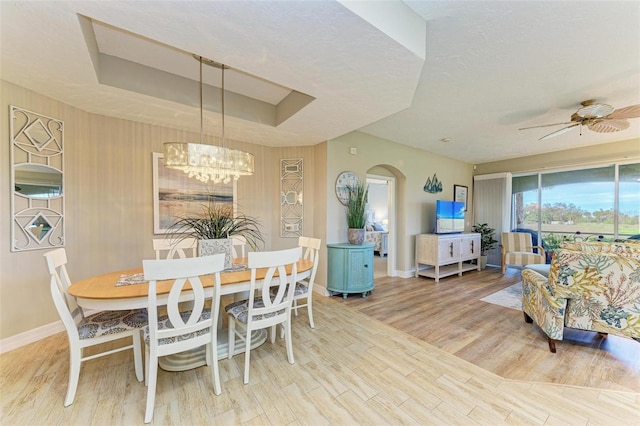 dining space featuring a textured ceiling, ceiling fan with notable chandelier, hardwood / wood-style floors, and a tray ceiling