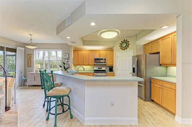 kitchen with decorative light fixtures, light hardwood / wood-style floors, a center island with sink, a breakfast bar, and appliances with stainless steel finishes