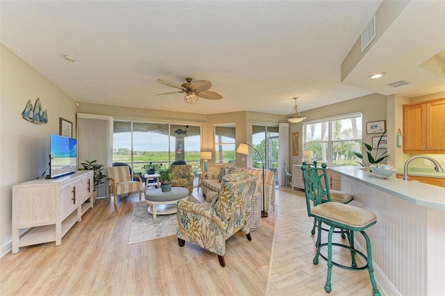 living room with ceiling fan, sink, and light wood-type flooring