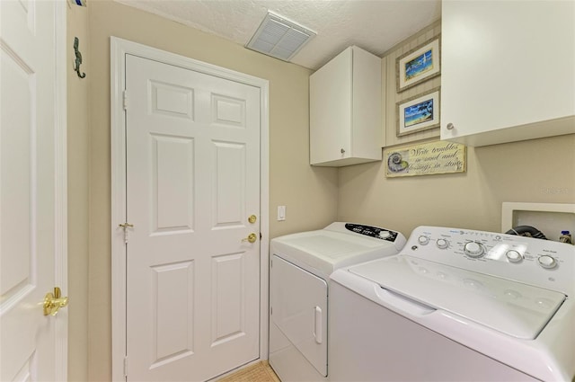 clothes washing area featuring washer and clothes dryer, a textured ceiling, and cabinets