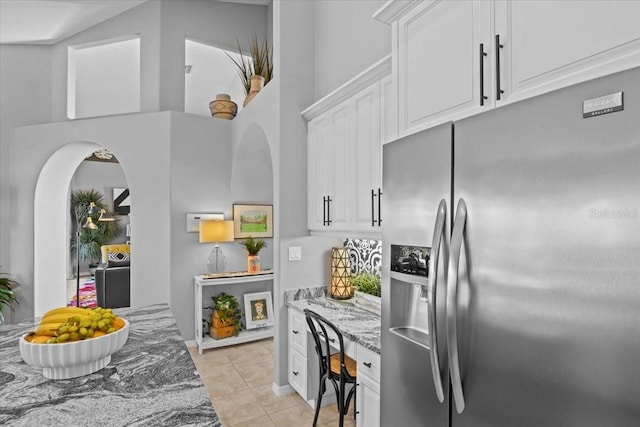 kitchen featuring stainless steel fridge, white cabinets, light stone countertops, and light tile patterned floors