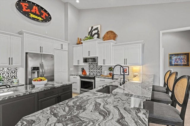 kitchen featuring white cabinetry, light stone countertops, a kitchen breakfast bar, backsplash, and appliances with stainless steel finishes