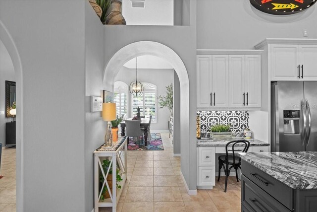 kitchen featuring stone countertops, an inviting chandelier, stainless steel fridge with ice dispenser, white cabinetry, and light tile patterned flooring