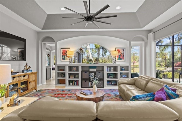 living room with a tray ceiling, a wealth of natural light, and ceiling fan