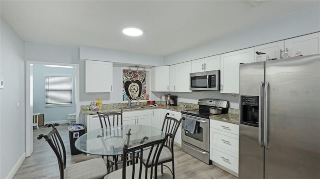 kitchen featuring white cabinetry, stainless steel appliances, dark stone counters, and light wood-type flooring