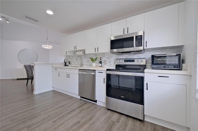 kitchen featuring white cabinets, decorative backsplash, hanging light fixtures, and appliances with stainless steel finishes