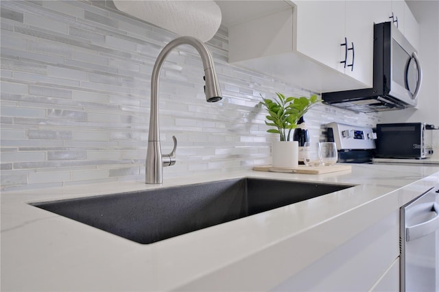 kitchen with stove, sink, decorative backsplash, light stone counters, and white cabinetry