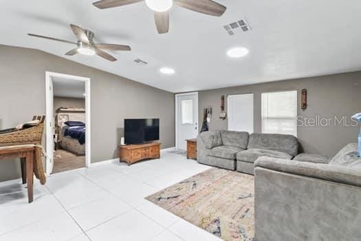 tiled living room with a wealth of natural light, ceiling fan, and vaulted ceiling