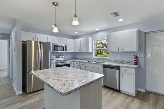 kitchen with appliances with stainless steel finishes, decorative light fixtures, white cabinets, a center island, and light hardwood / wood-style floors