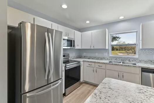 kitchen featuring light stone countertops, sink, stainless steel appliances, light hardwood / wood-style flooring, and white cabinets