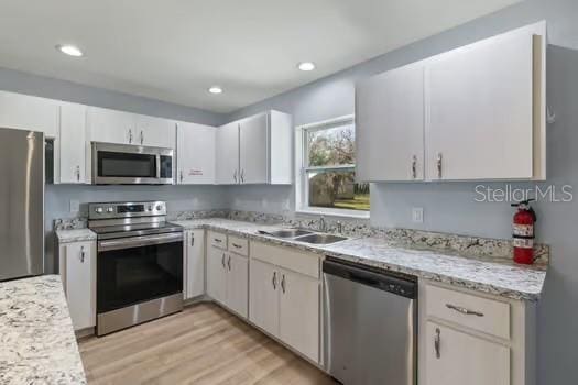 kitchen featuring white cabinetry, sink, stainless steel appliances, light stone counters, and light hardwood / wood-style floors