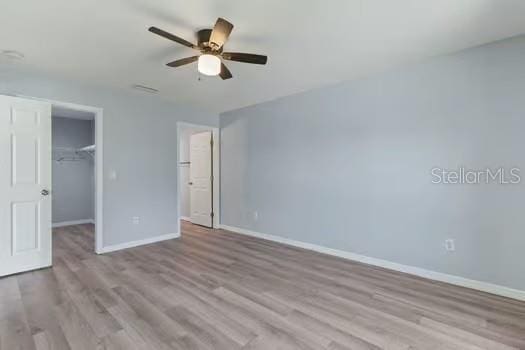 unfurnished bedroom with a closet, a spacious closet, ceiling fan, and light hardwood / wood-style floors