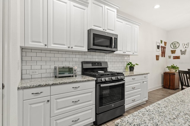 kitchen with light hardwood / wood-style floors, stainless steel appliances, light stone countertops, white cabinetry, and backsplash