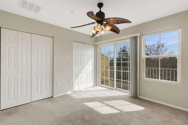 unfurnished bedroom with two closets, light colored carpet, access to exterior, and ceiling fan